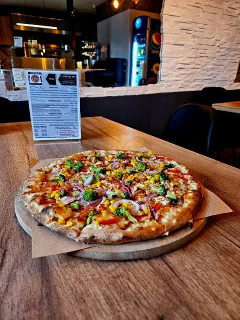 Pizza Letnia Fantazja: kebab drobiowy, brokuły, papryka, kukurydza i czerwona cebula, na stoliku w lokalu